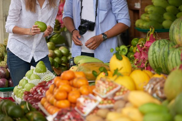 Young interracial couple of tourists choosing fresh fruits at street market